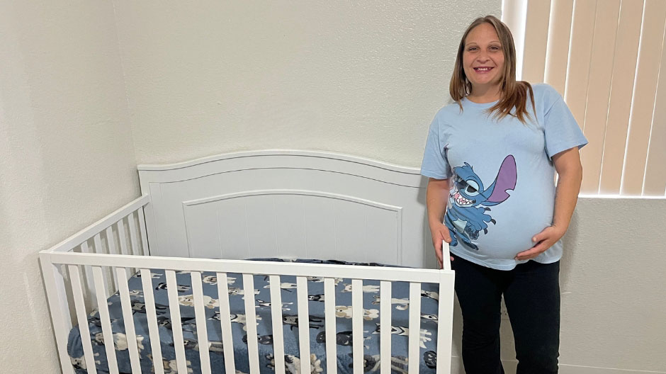 Pregnant woman in a light blue graphic tee standing next to a white crib.