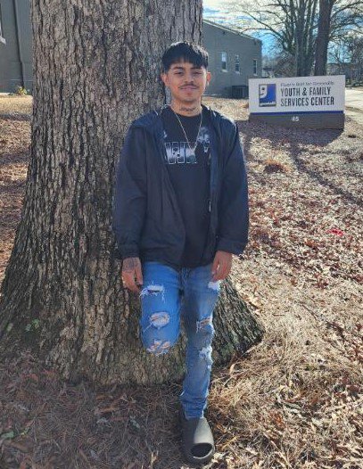 Rodmam, a 20-year-old, leans against a tree with a “Goodwill Industries” sign in the background