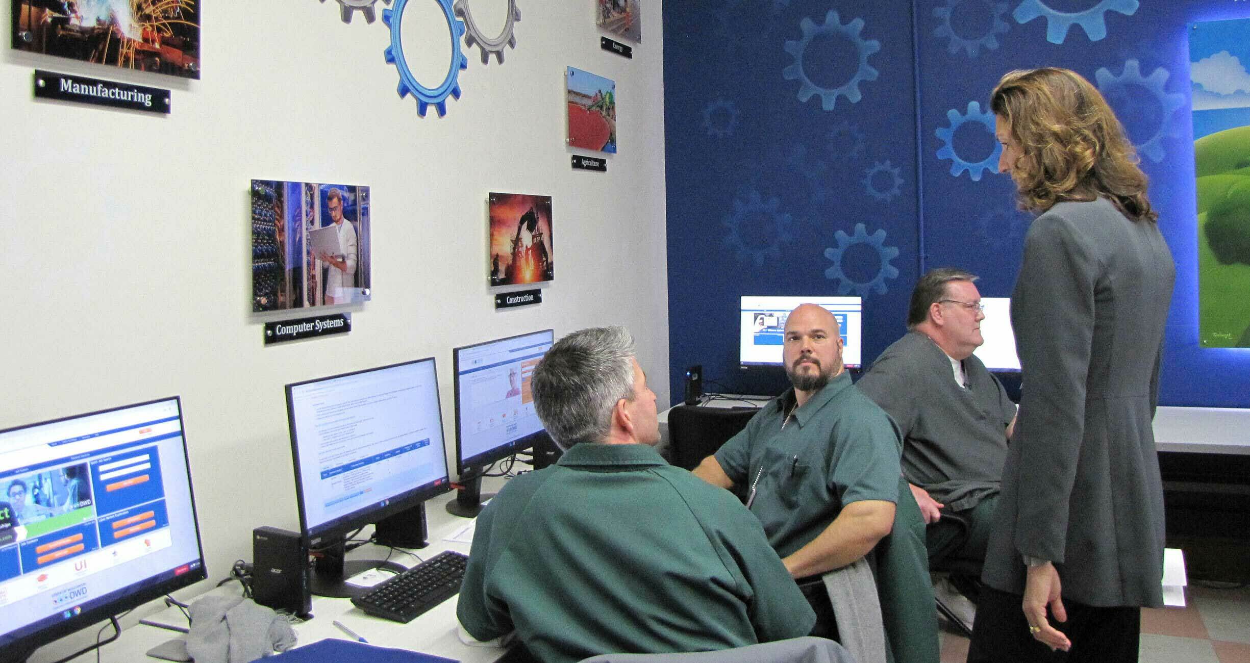 Men sitting at computers talking with a woman