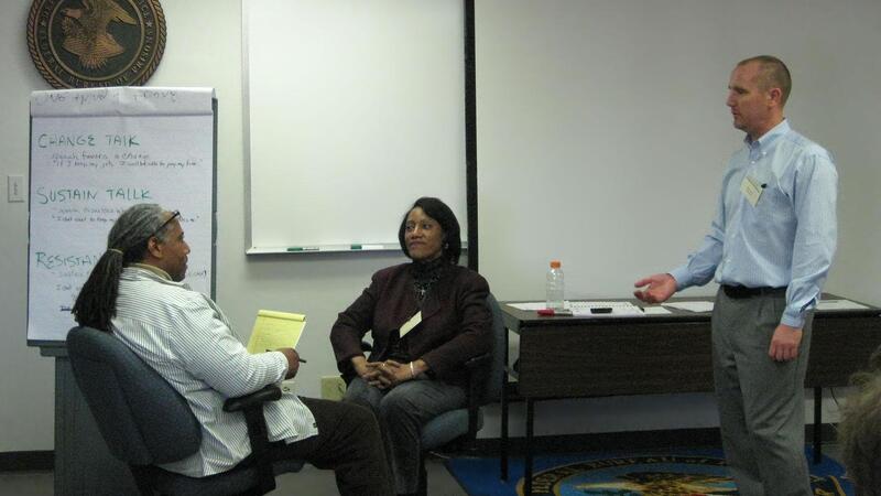 Two people seated next to another person standing in a classroom