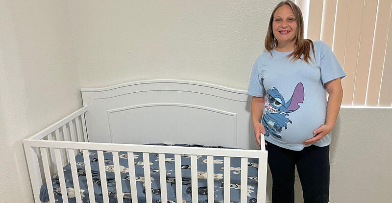 Pregnant woman in a light blue graphic tee standing next to a white crib.