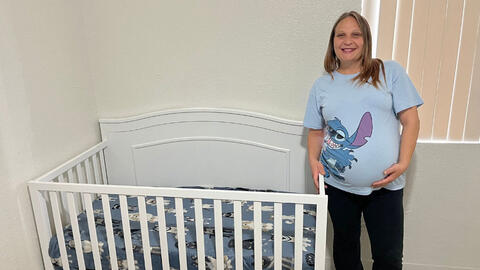Pregnant woman in a light blue graphic tee standing next to a white crib.